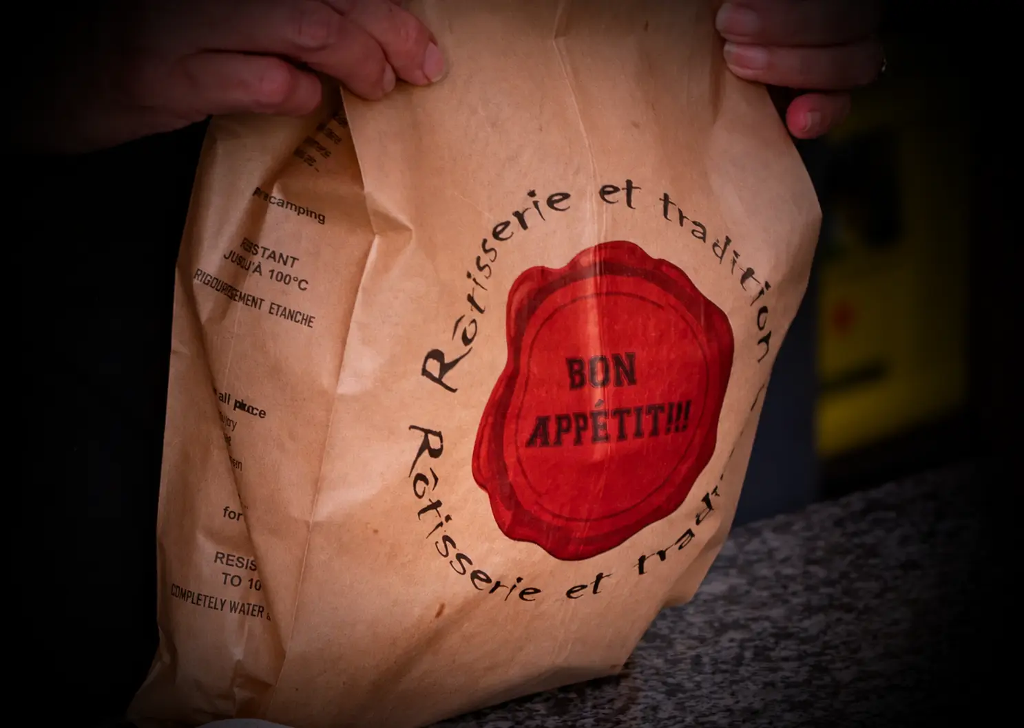 Sac kraft de la rôtisserie marqué « Bon appétit », tenu à deux mains au-dessus du comptoir