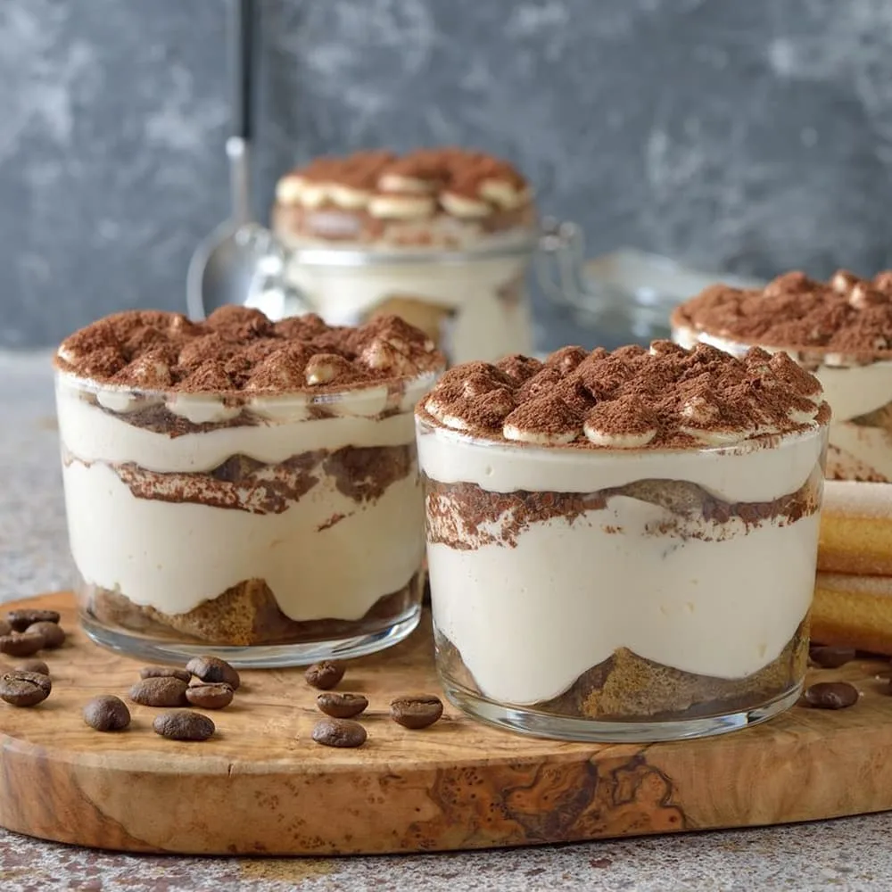 Tiramisus en verrines saupoudrés de cacao, sur une planche en bois