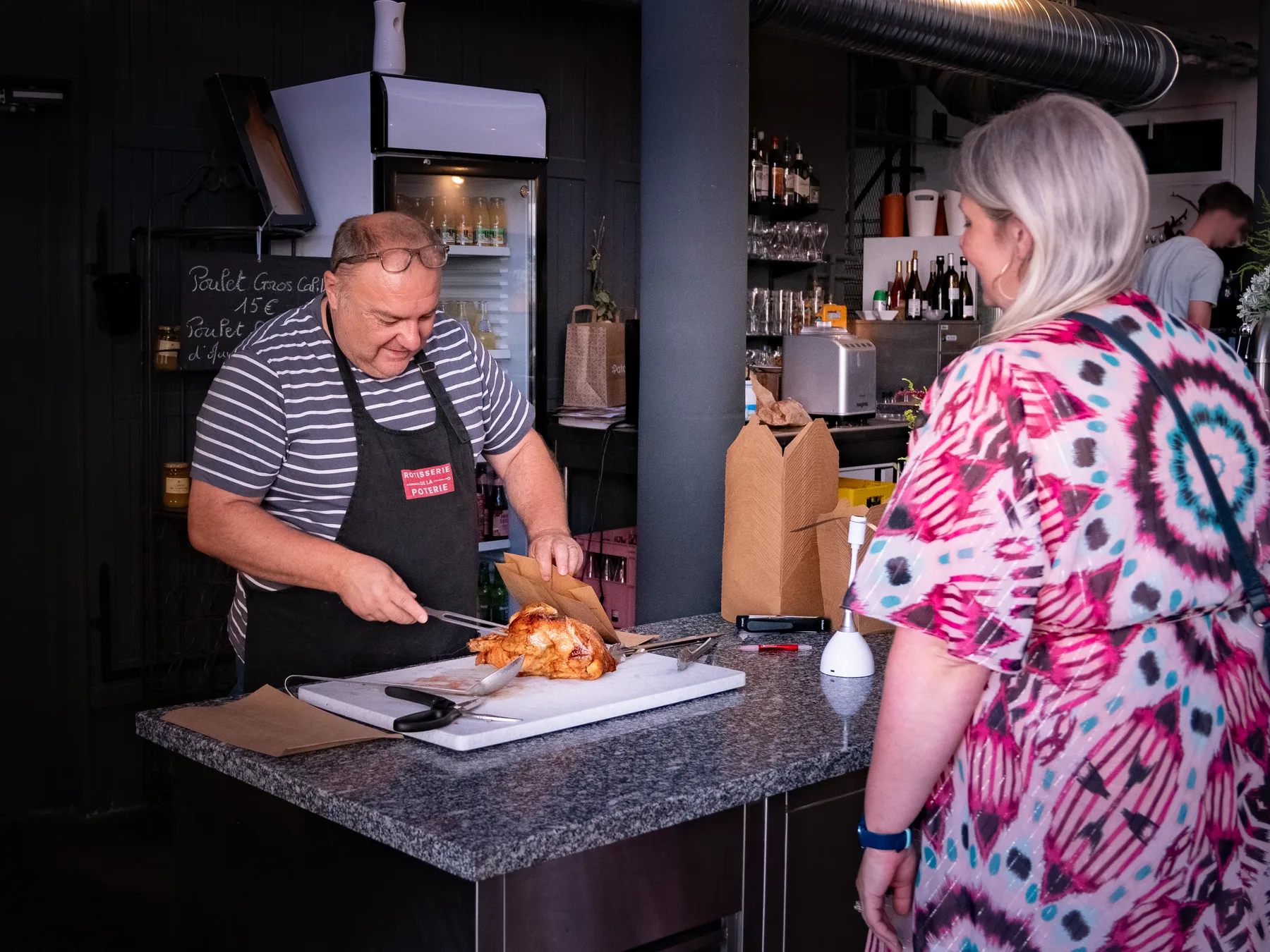 Vincent découpe un poulet rôti au comptoir, une cliente lui fait face