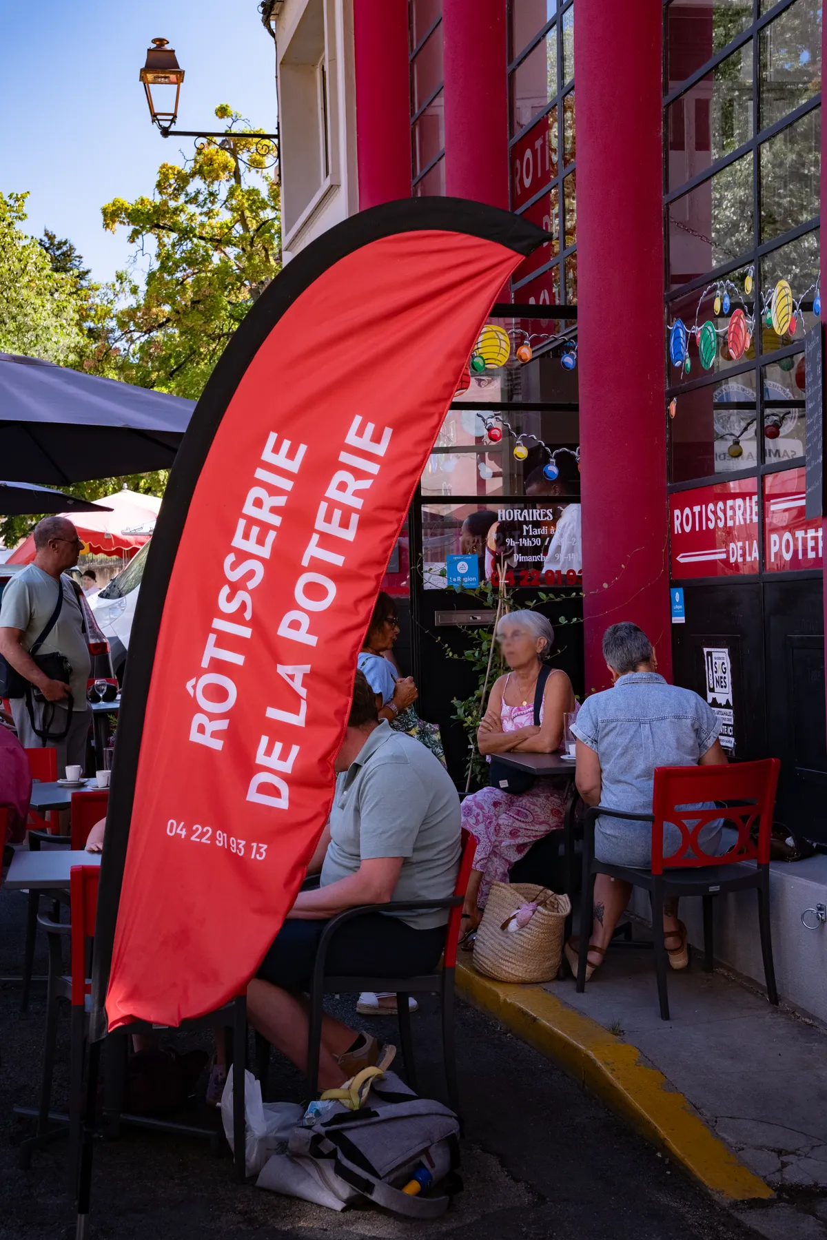 Le drapeau rouge Rôtisserie de la Poterie devant la terrasse, clients attablés sous les guirlandes