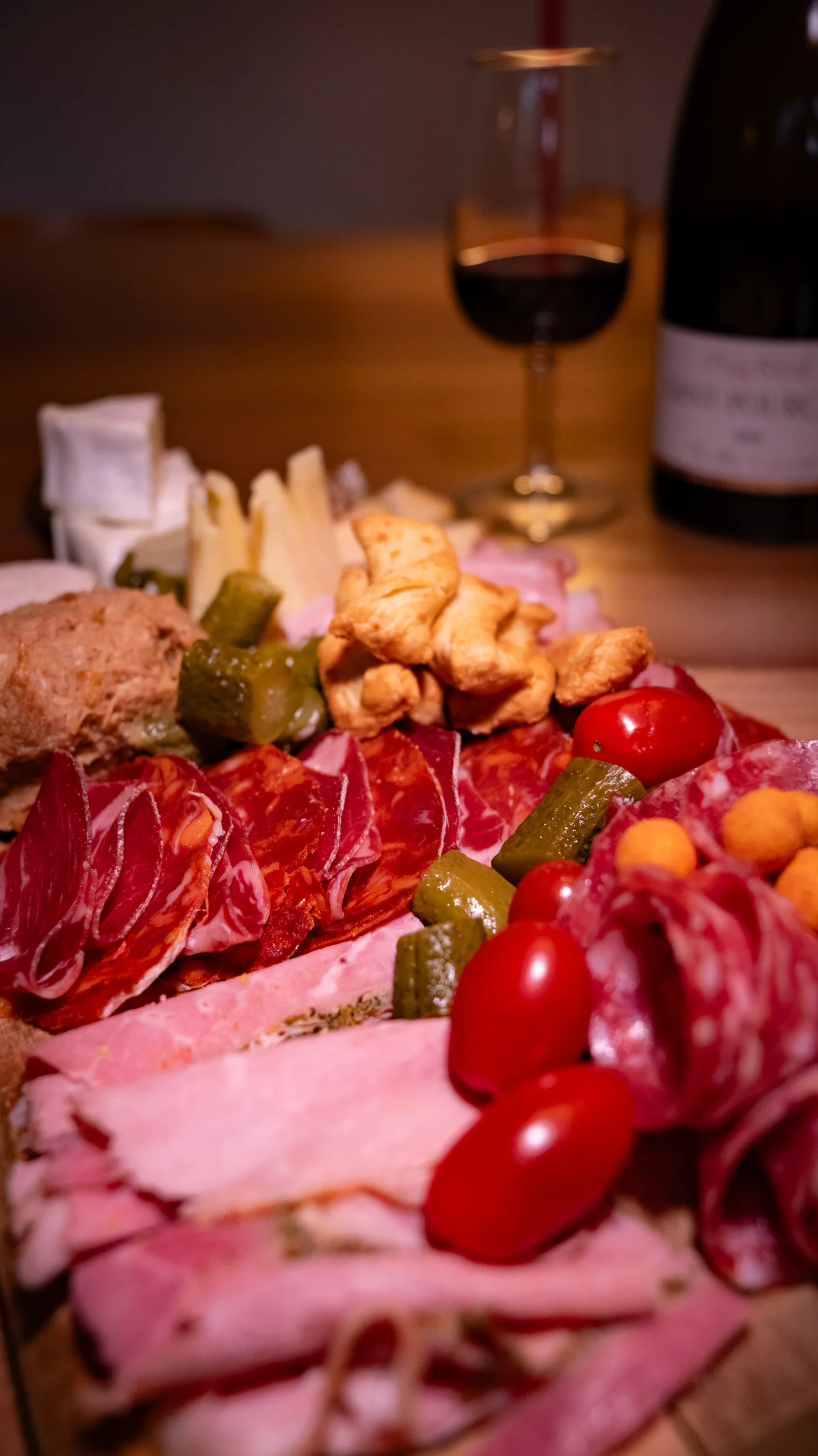 Planche apéro : charcuteries, fromages, cornichons et tomates cerises, verre de vin rouge