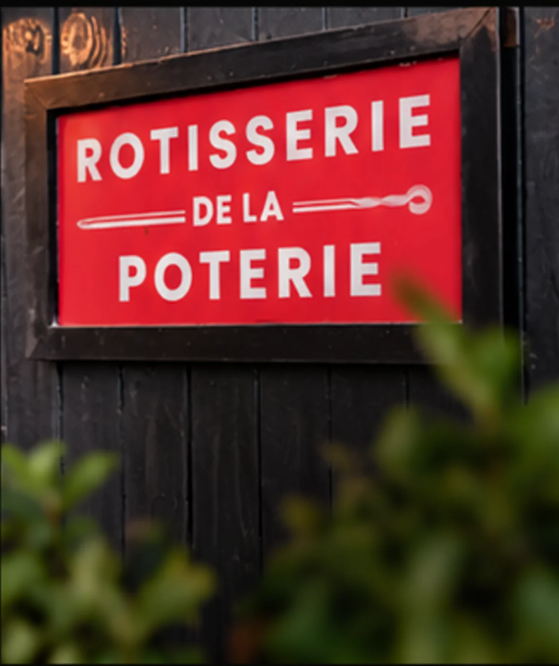 Enseigne rouge Rôtisserie de la Poterie encadrée de bois, sur un bardage noir