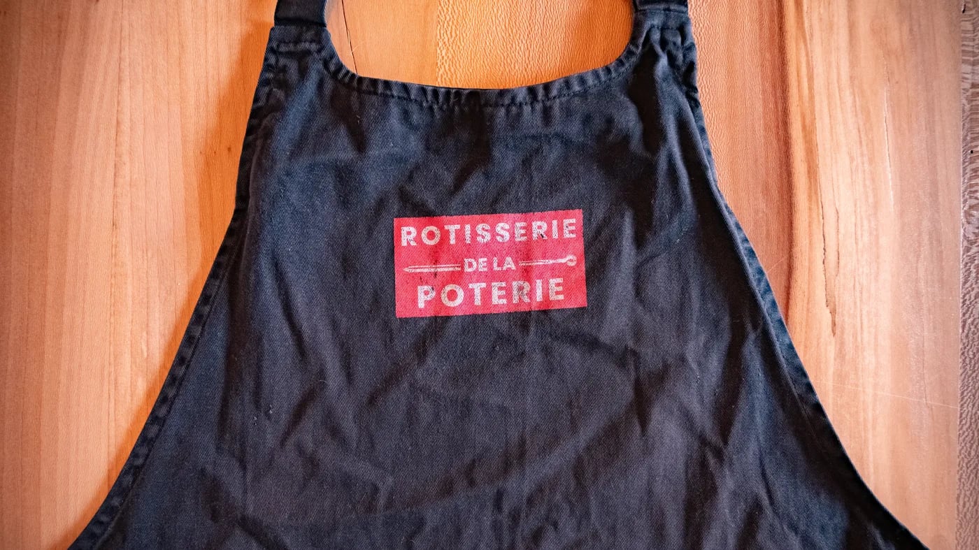 Tablier noir Rôtisserie de la Poterie posé sur une planche en bois