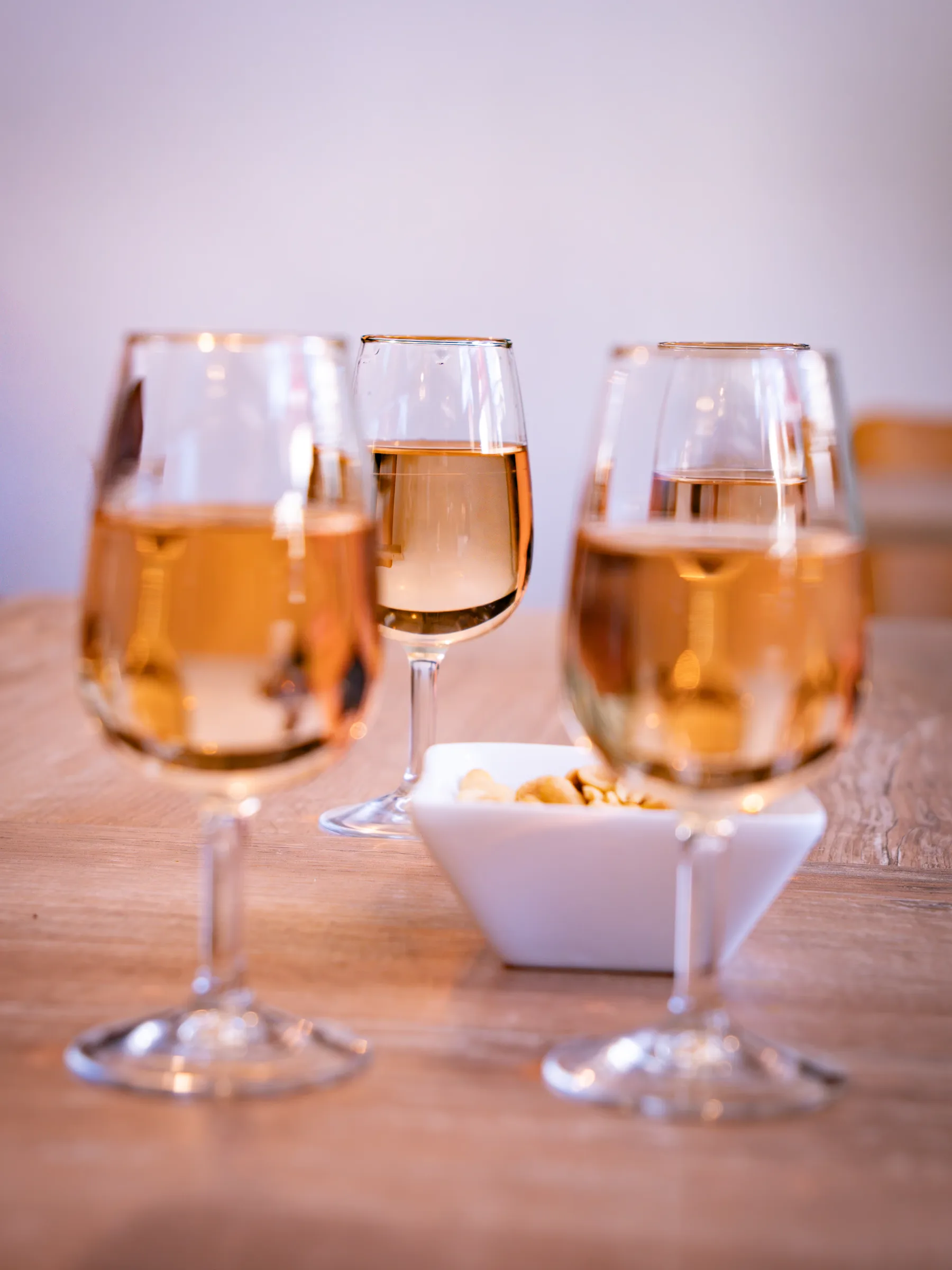 Trois verres de vin blanc et une coupelle de cacahuètes sur une table en bois